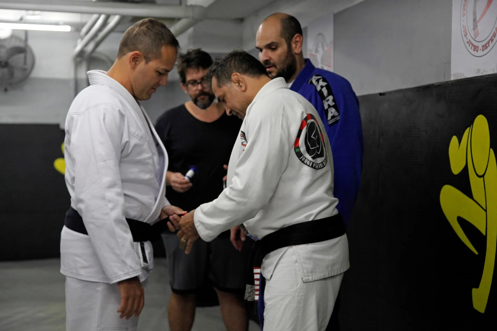 A stripe being placed on Fabiano's black belt by his instructor while training partners look on