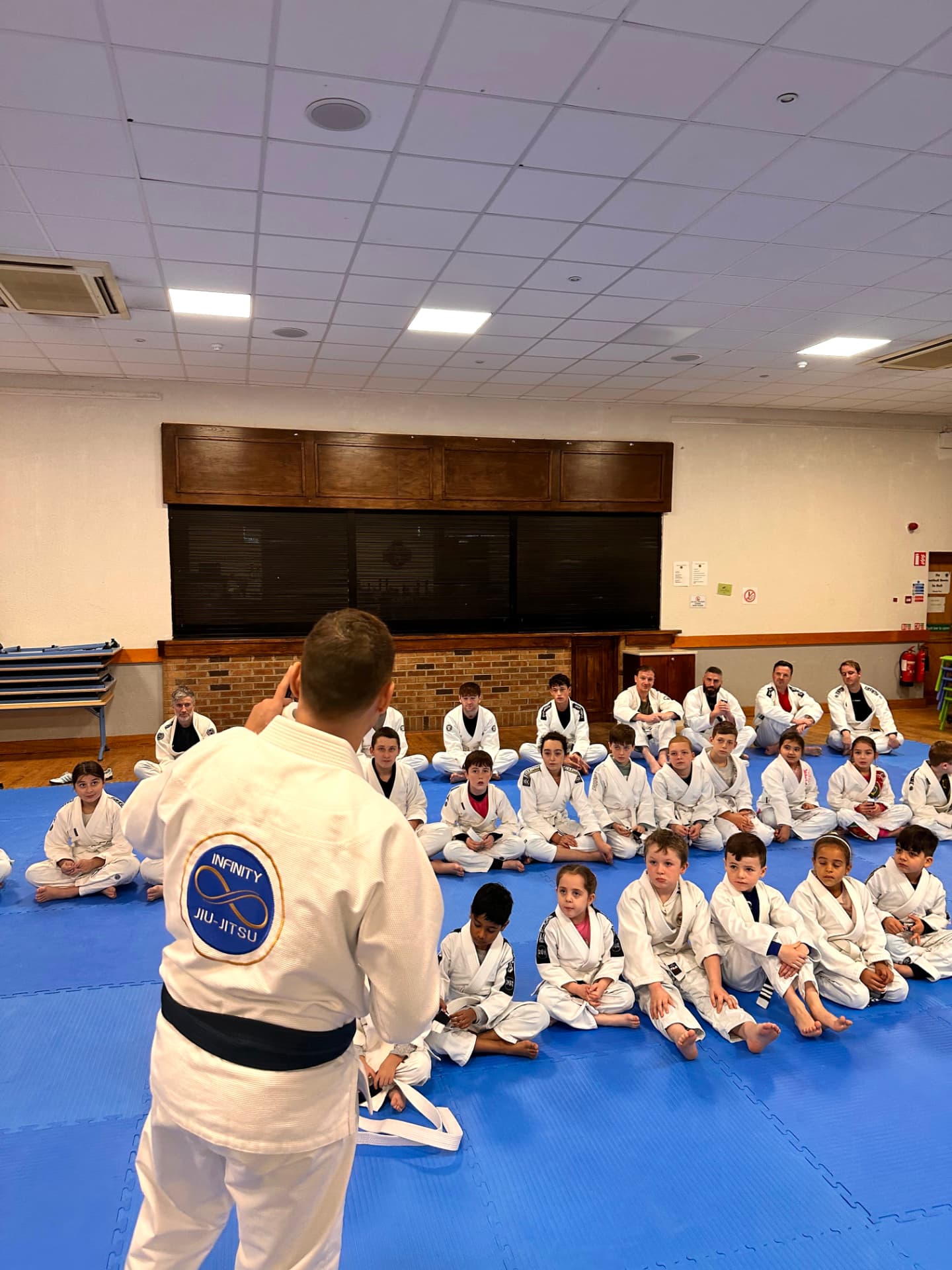 A large group photograph of Infinity Jiu-Jitsu children, parents and adult students together on the mats