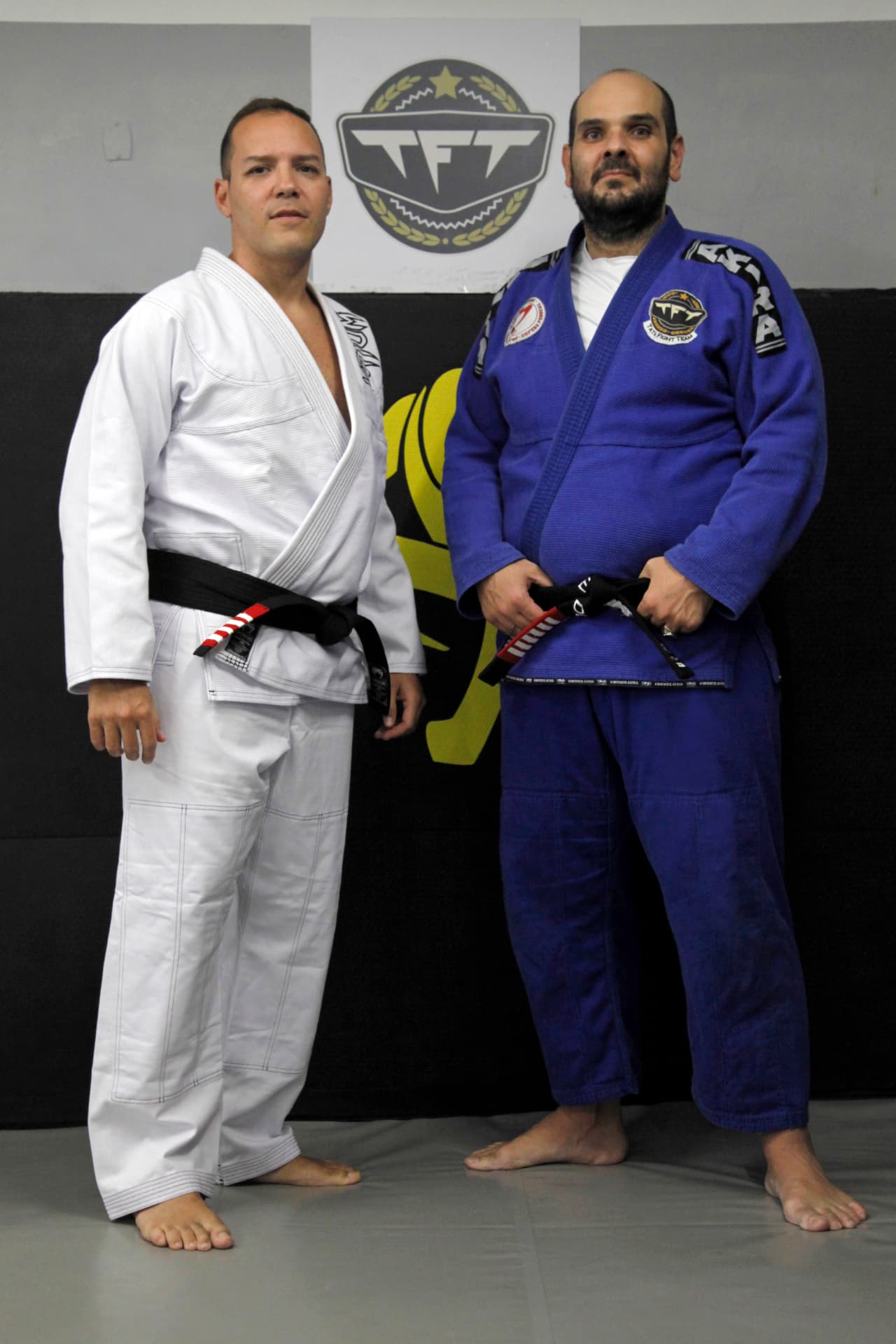 Fabiano in a white gi standing beside a black belt instructor in a blue gi at the academy