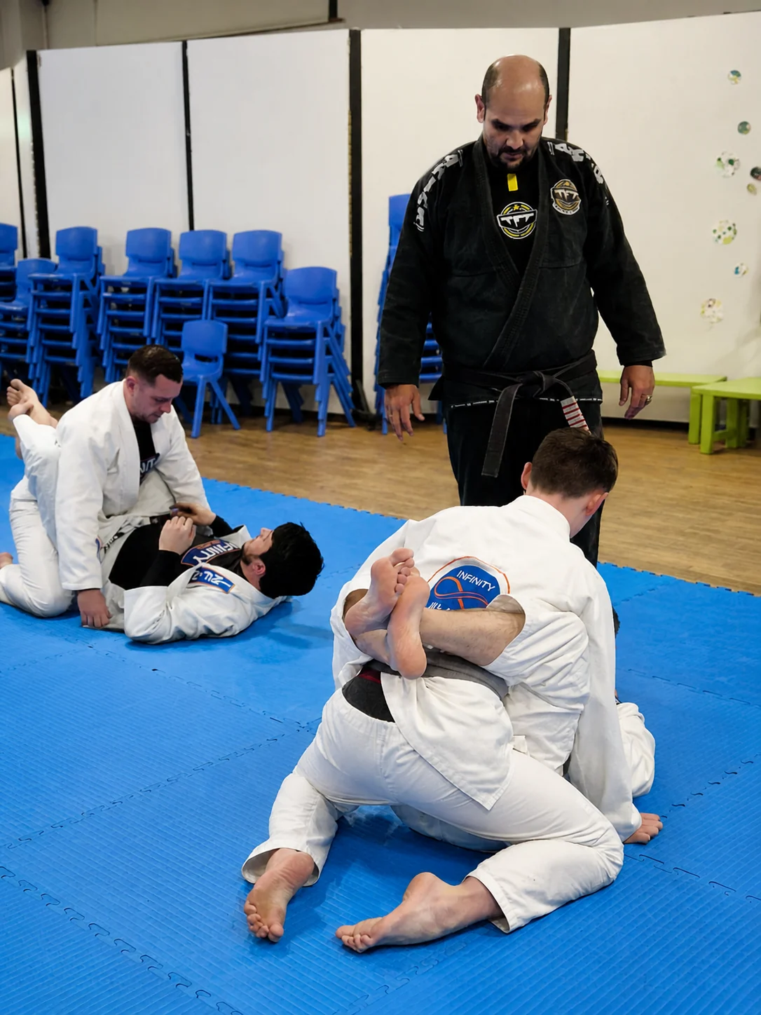 Visiting black-belt instructor Professor Otávio “Tatá” Duarte standing on the mats watching adult students drill during a seminar at Infinity Jiu-Jitsu