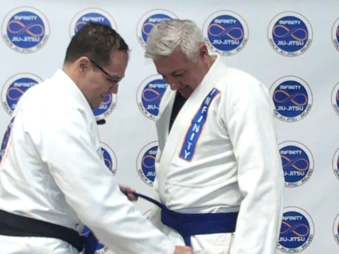 Professor Fabiano tying a new blue belt on a student while the class watches