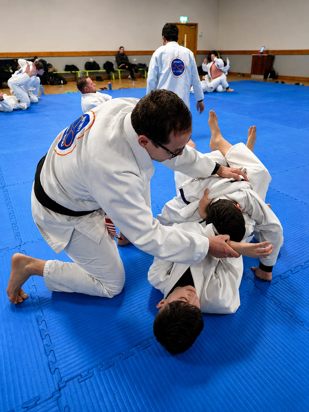 Professor Fabiano kneeling on the mats to help a young student with a technique during a class at Infinity Jiu-Jitsu