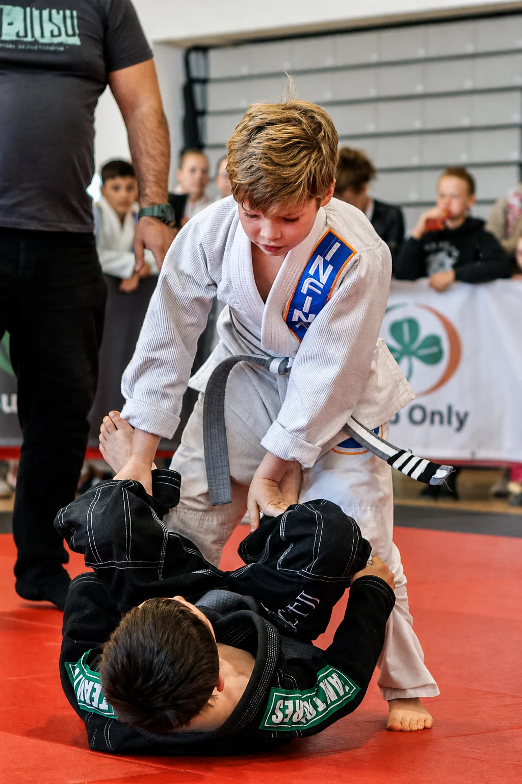 An Infinity Jiu-Jitsu student in a white gi passing the guard of an opponent in a black gi at a competition