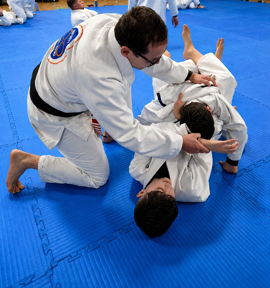 Professor Fabiano guiding two young students through a technique on the mats at Infinity Jiu-Jitsu