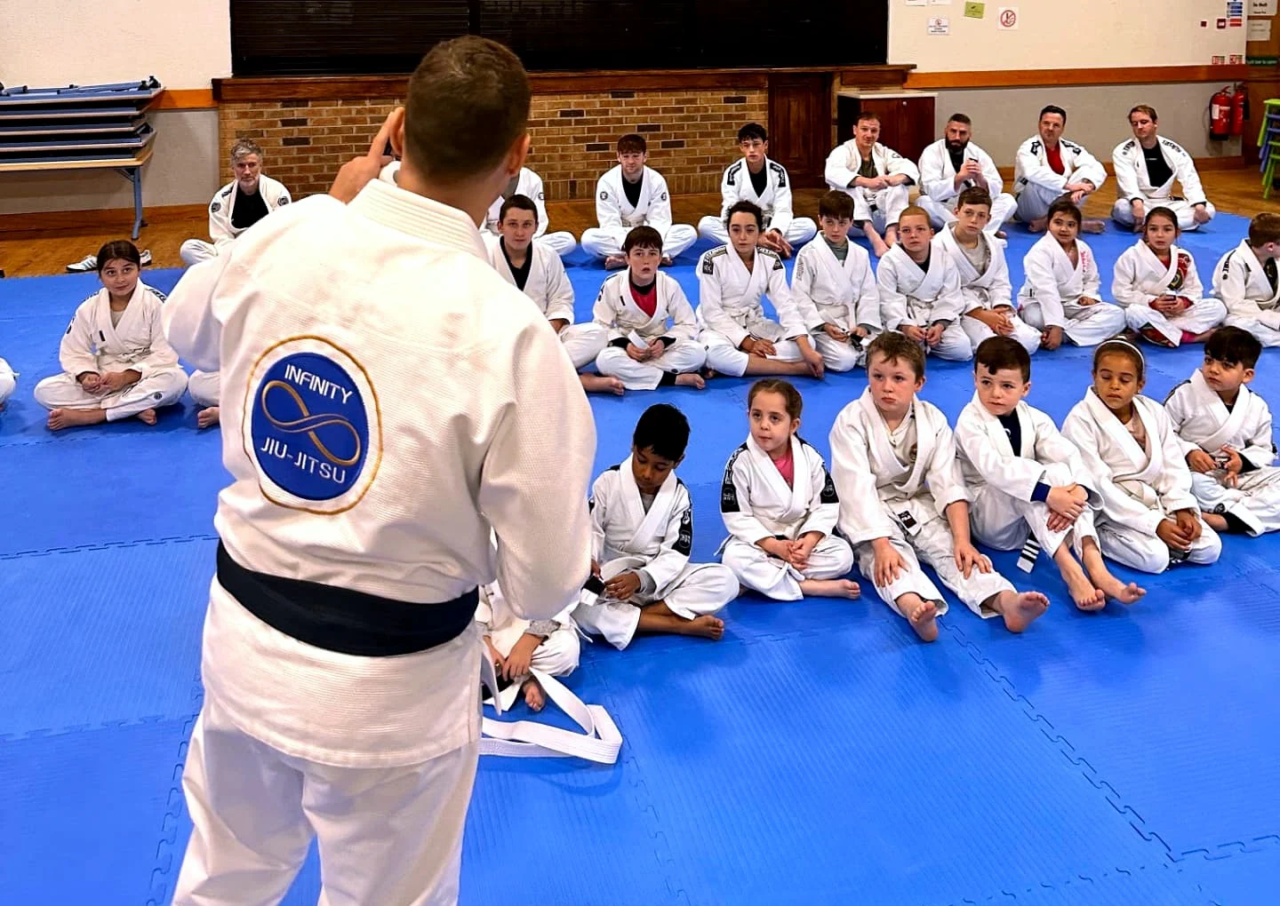 Infinity Jiu-Jitsu students sitting together on the mats at the start of a class