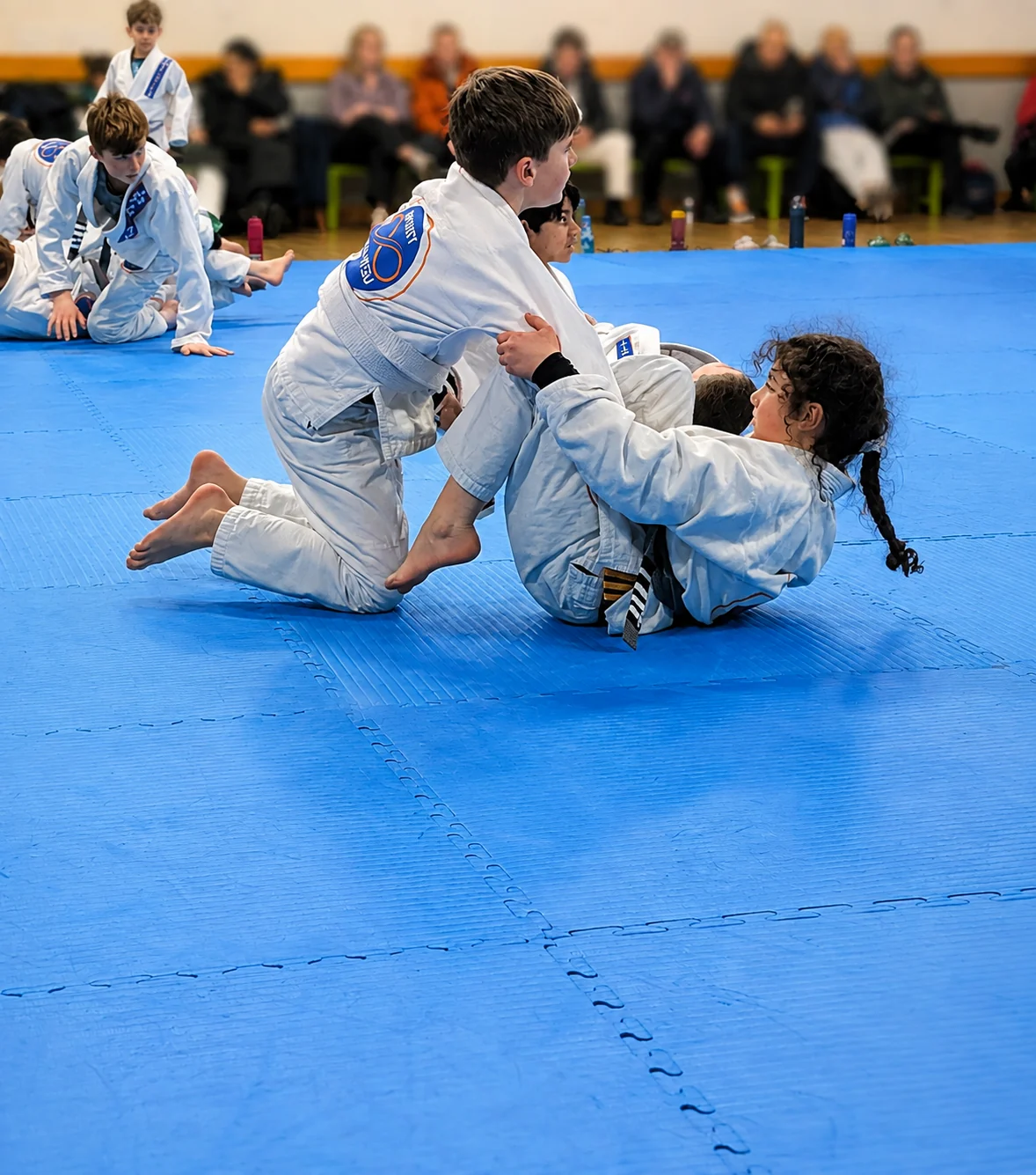 Junior Academy students training on the mats while parents watch from the side