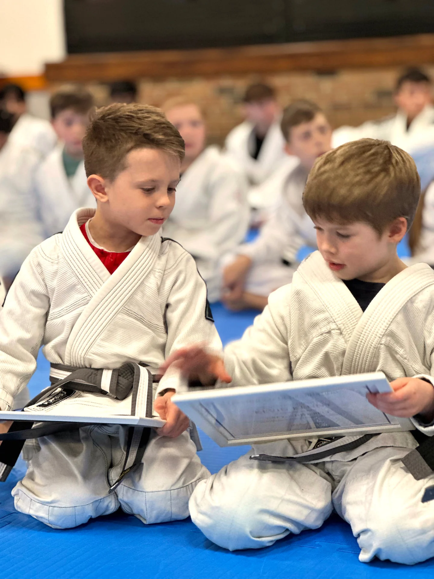 Two young Infinity Jiu-Jitsu students sitting on the mats together during a Little Champions class